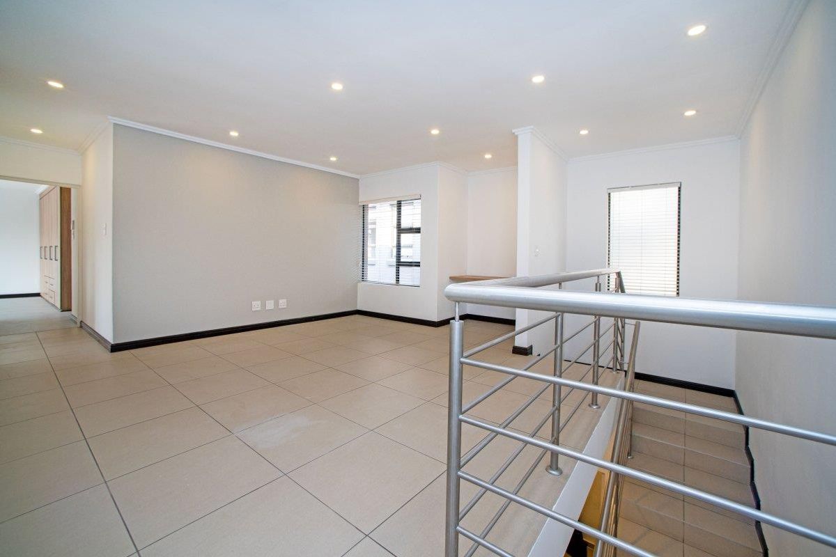 An open-plan living area featuring neutral tiled flooring, recessed downlights, a stainless steel balustrade, and a convenient built-in desk nook.