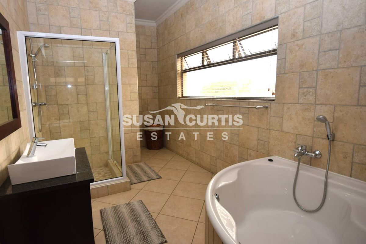 A well-maintained bathroom featuring floor-to-ceiling stone tiling, a glass-enclosed shower, a corner bathtub, and a modern vanity basin.