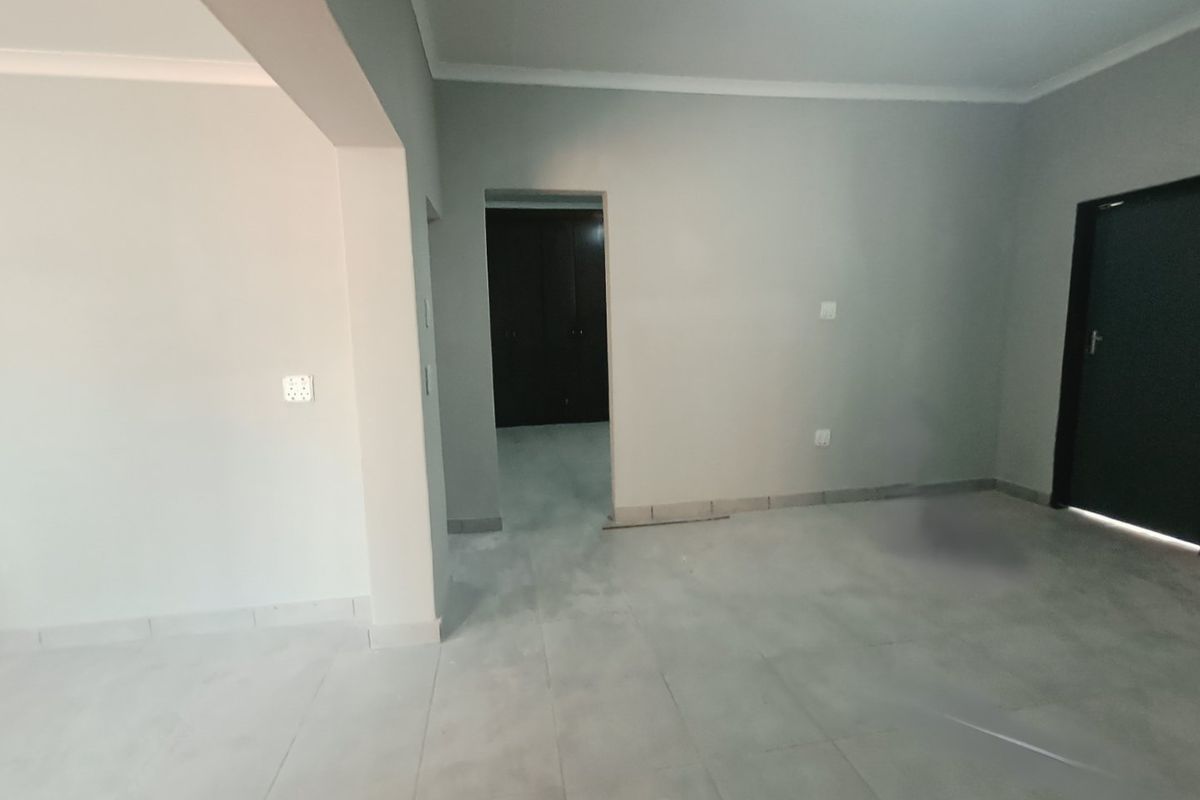 An empty, open-plan living area featuring neutral tiled flooring, cove cornicing, and access to a room with built-in cupboards.