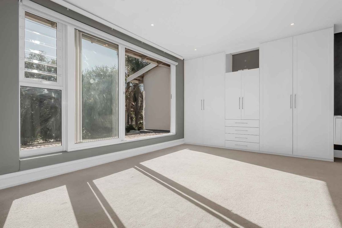 Bright bedroom featuring large windows, neutral carpeting, and extensive built-in white cabinetry providing ample storage space.