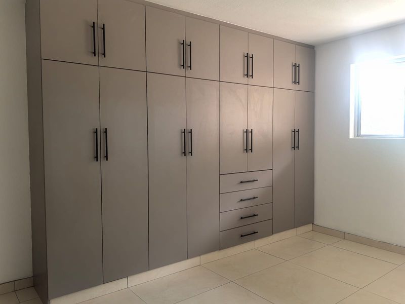A bright, empty bedroom featuring extensive floor-to-ceiling built-in cabinetry with modern matte finishes and tiled flooring.