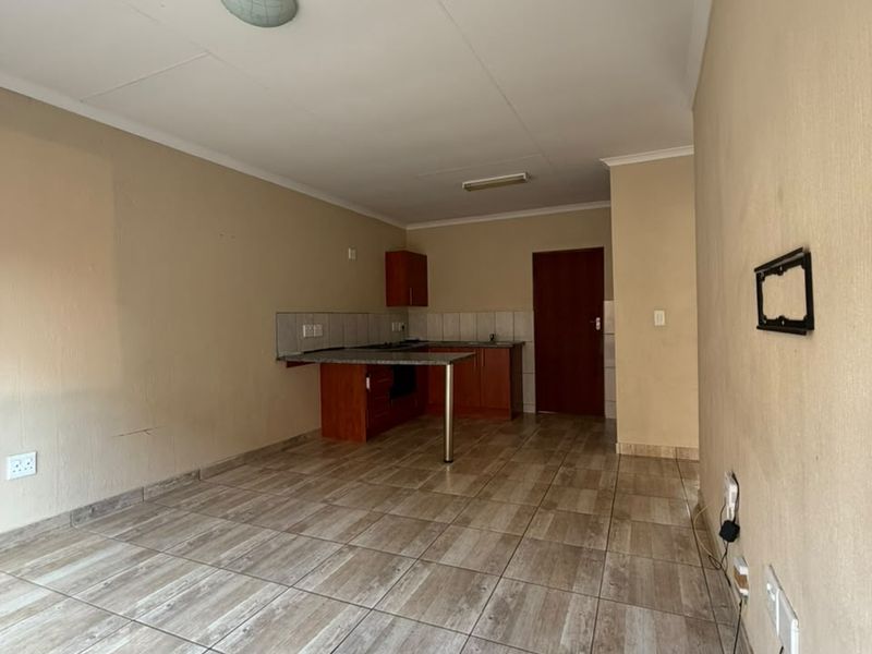 An open-plan living and kitchen area featuring tiled flooring, built-in cabinetry with granite countertops, and neutral wall finishes in a vacant space.