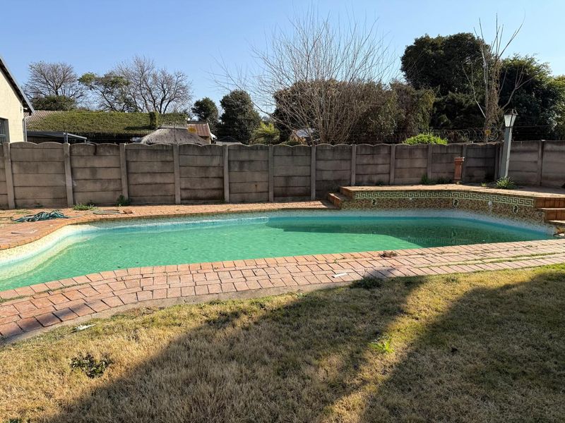 Outdoor swimming pool area featuring brick paving and a precast concrete boundary wall, requiring maintenance to the pool water and surrounding landscaping.