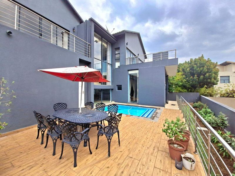 A modern double-storey home exterior featuring a tiled patio deck, a swimming pool, and stainless steel balustrades.