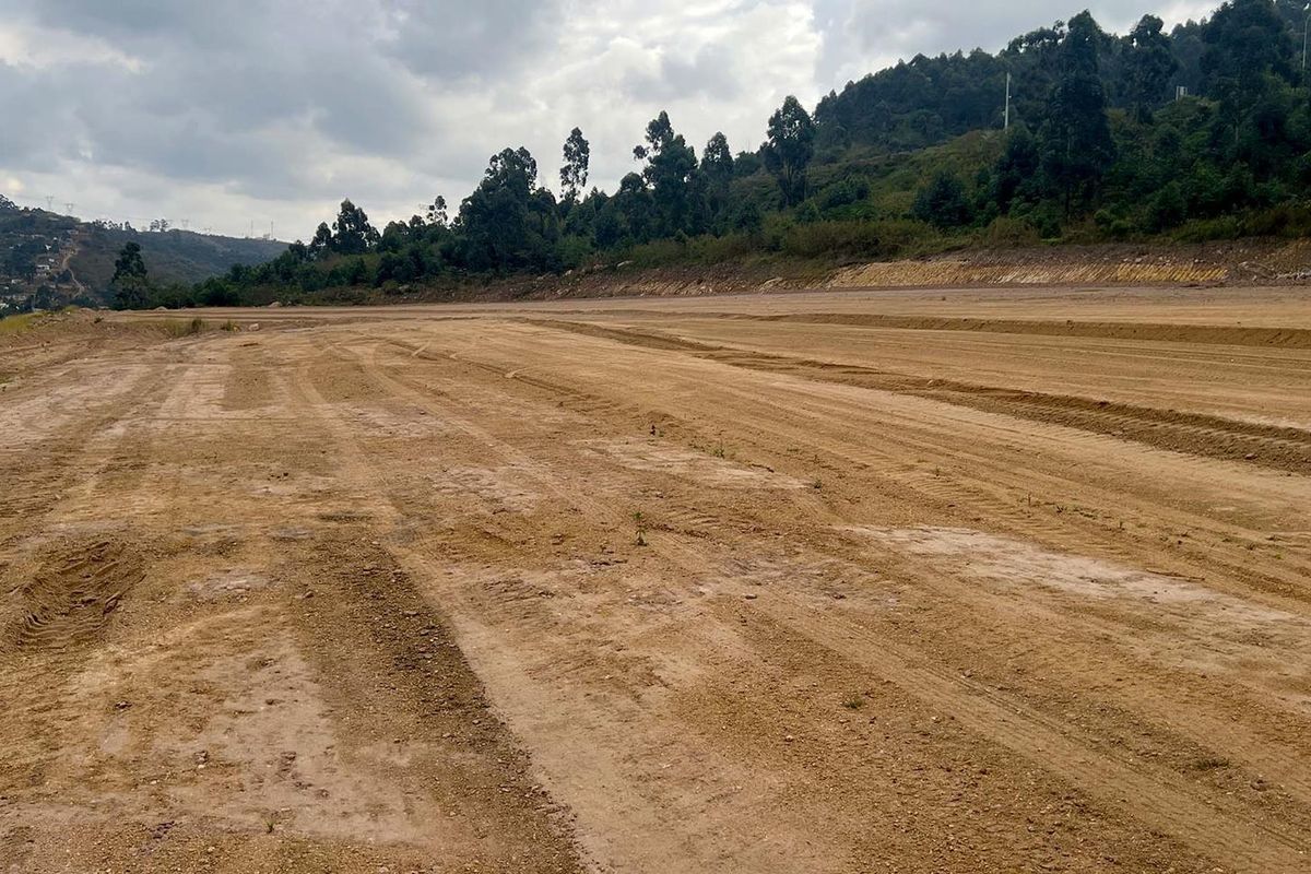 A wide-angle view of a large, cleared commercial vacant land plot with leveled earth and surrounding hillside terrain.