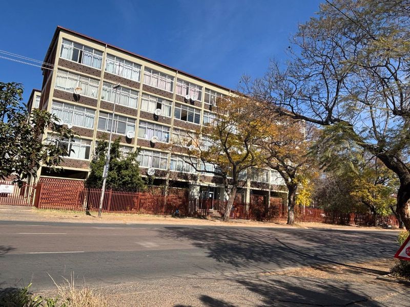 Street-level view of a multi-story brick apartment building featuring large windows and secure perimeter fencing.