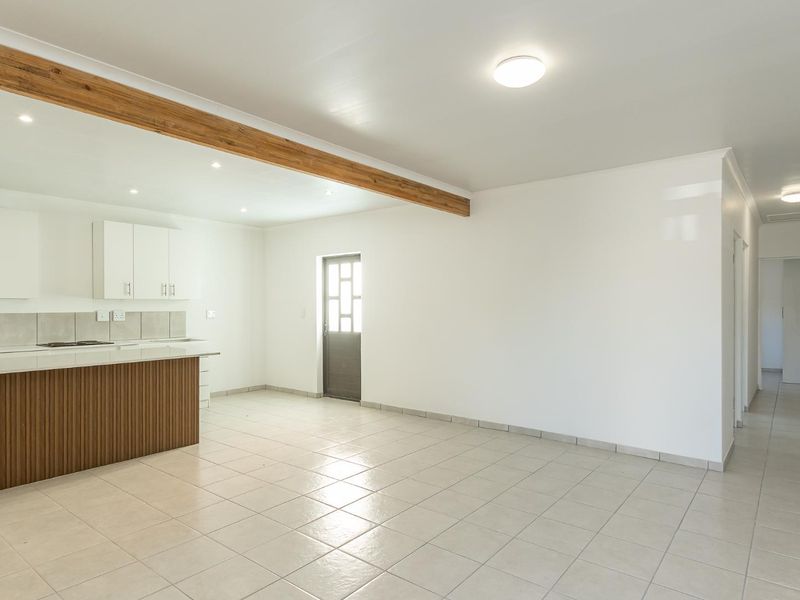 Spacious open-plan living and kitchen area featuring tiled floors, a central timber beam, and modern white cabinetry with a built-in hob.
