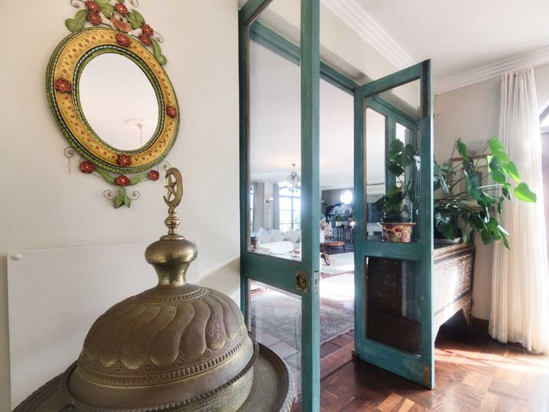 A welcoming hallway featuring rich parquet flooring and distinctive teal-painted glass panelled doors leading into the main living area.
