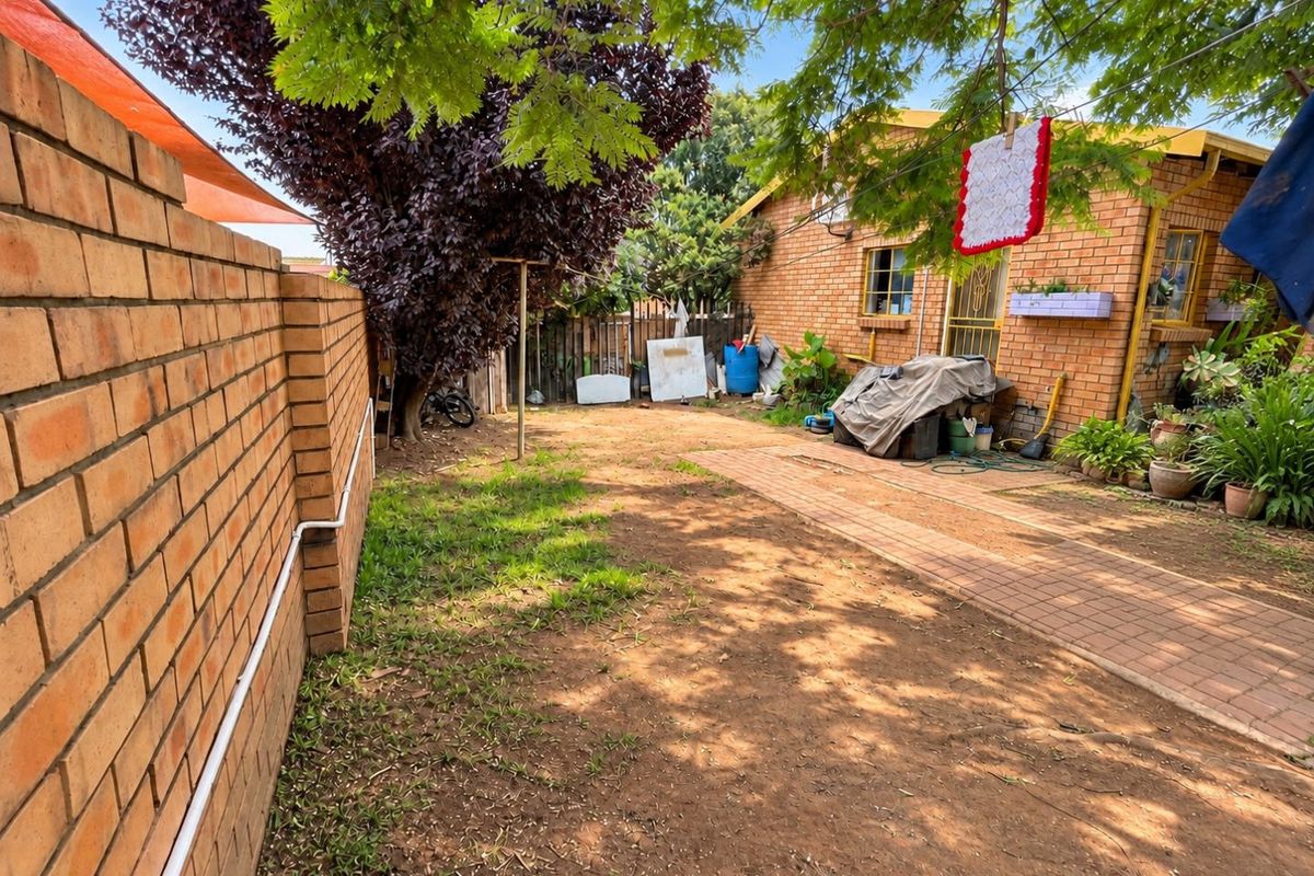 Rear garden area featuring a brick boundary wall, paved walkway, and face brick exterior wall of the house.