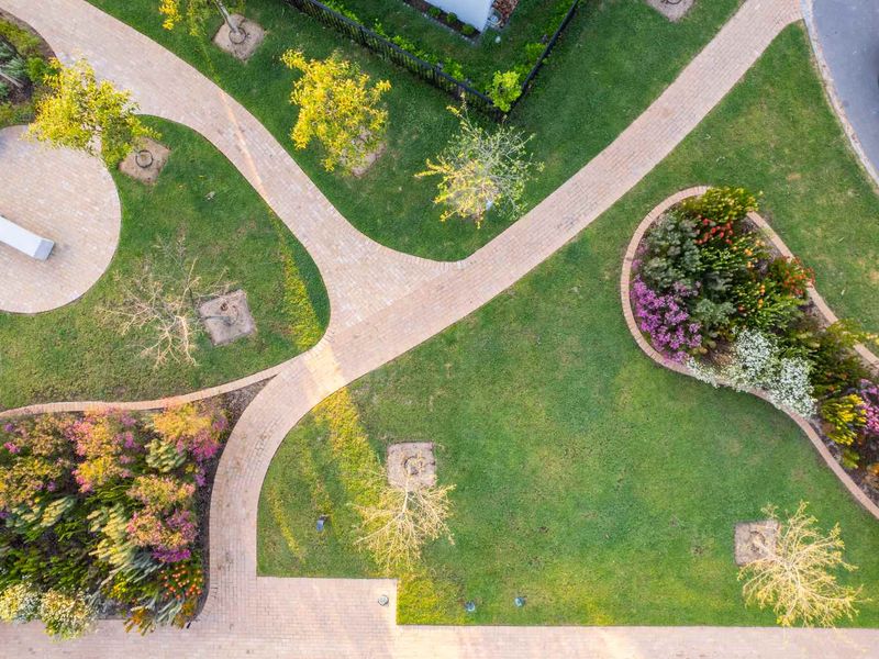 An aerial view of a well-maintained residential garden featuring paved pathways, manicured lawn areas, and established flower beds.