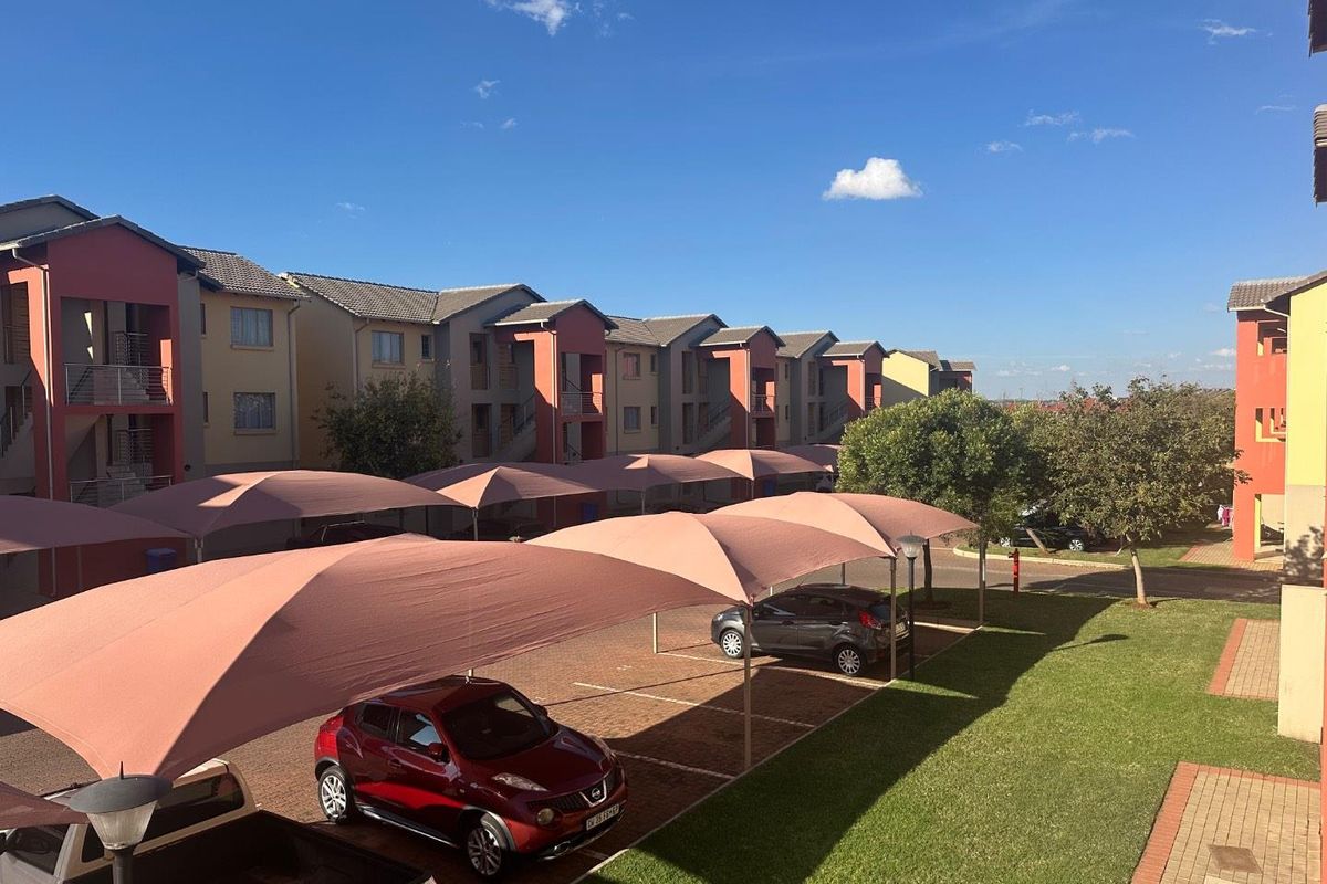View of the apartment complex parking area featuring covered shade-net carports and landscaped garden spaces.
