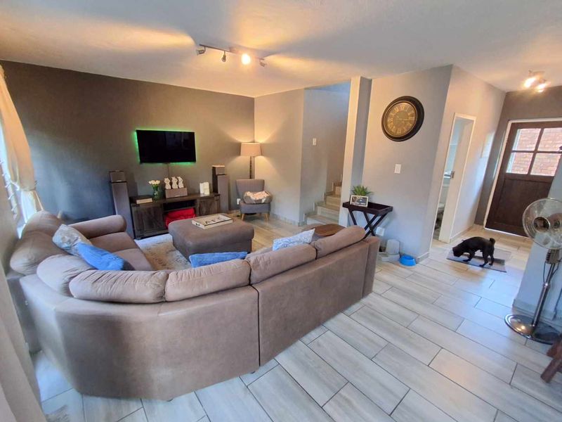 A well-maintained living room featuring modern tiled flooring, neutral wall tones, and an open-plan layout leading to the staircase and entrance.