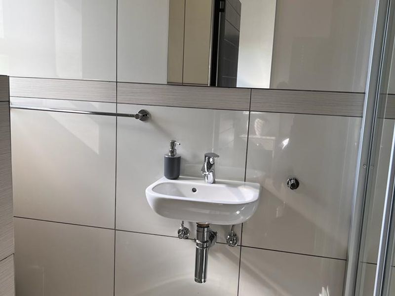 A modern bathroom featuring a wall-mounted basin, chrome fixtures, tiled walls, and a glass shower enclosure.