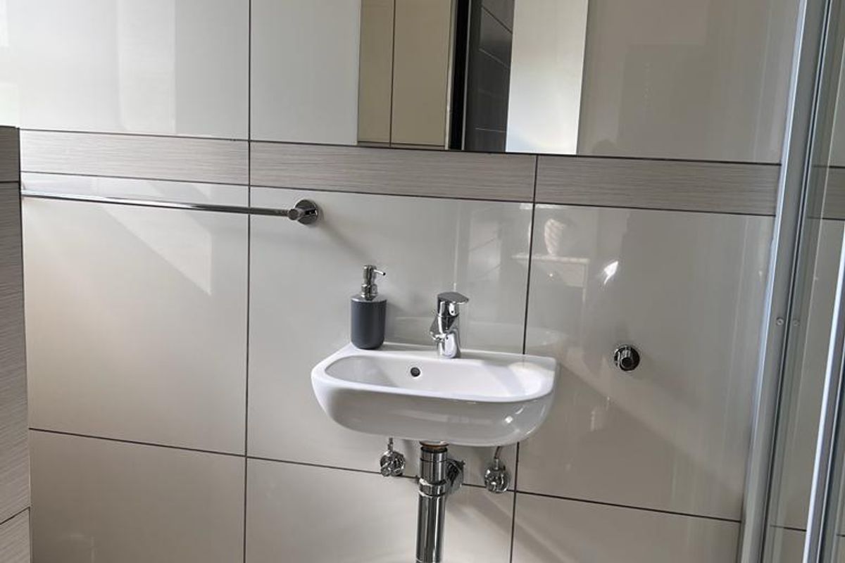 A modern bathroom featuring a wall-mounted basin, chrome fixtures, tiled walls, and a glass shower enclosure.