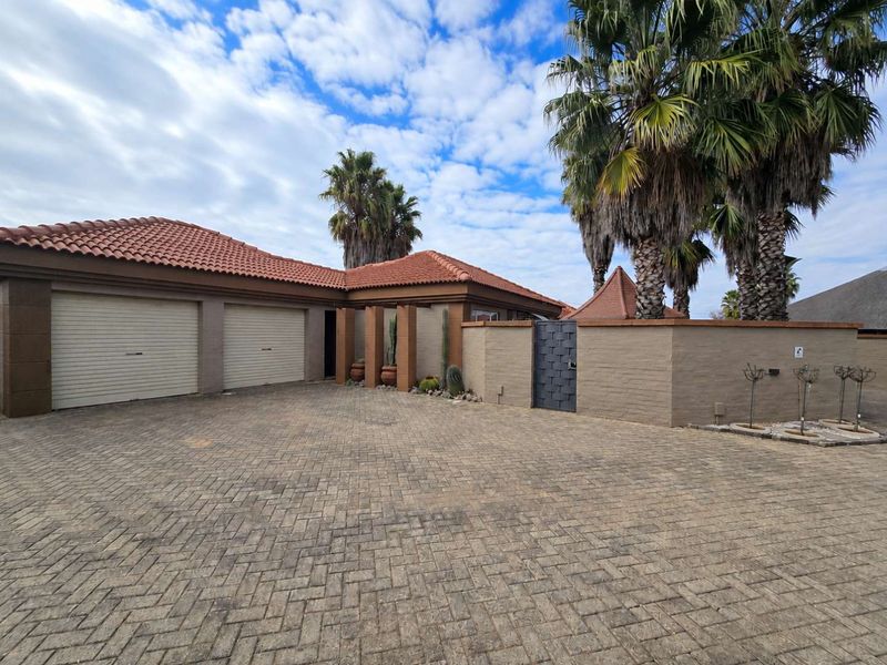 Front elevation of a townhouse featuring a paved driveway, double garage with roller shutter doors, and a secure pedestrian entrance gate.