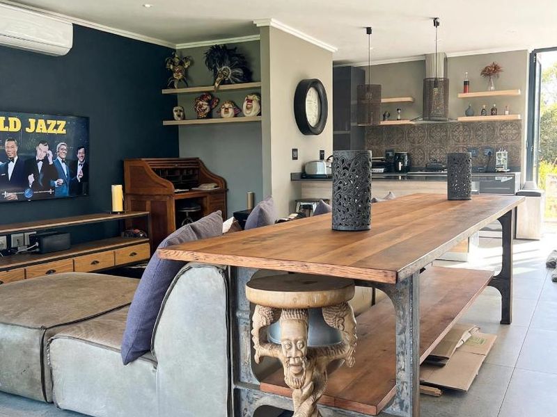 Spacious open-plan living and kitchen area featuring modern tiled floors, built-in shelving, and a stylish patterned backsplash, seamlessly connecting to outdoor space.
