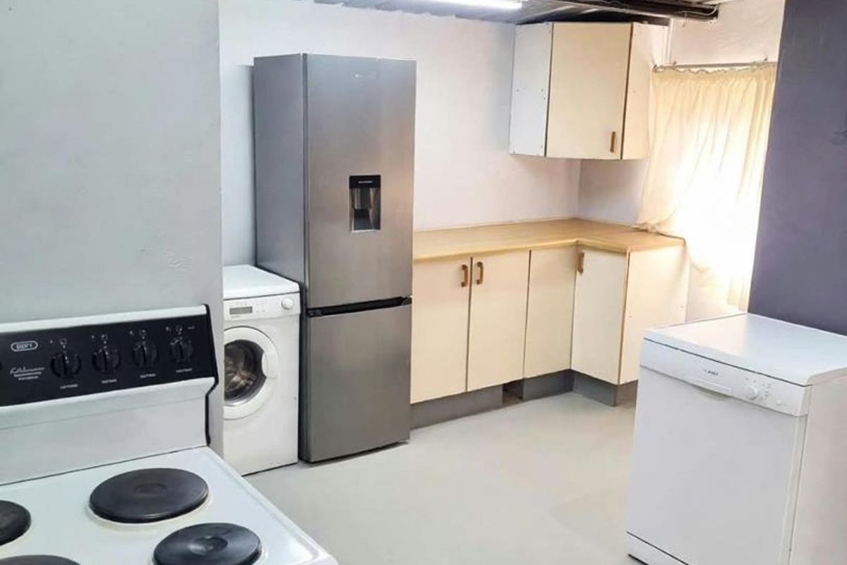 A functional kitchen area featuring built-in cabinetry, laminate countertops, and an exposed corrugated metal ceiling, providing a basic utility space.