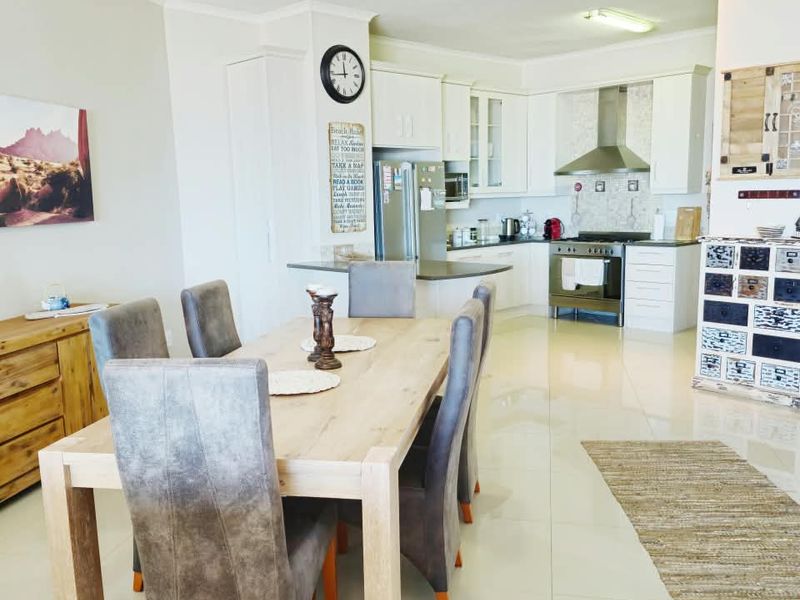 Spacious open-plan living and dining area featuring a modern kitchen with white cabinetry, stainless steel appliances, and polished tiled flooring throughout.