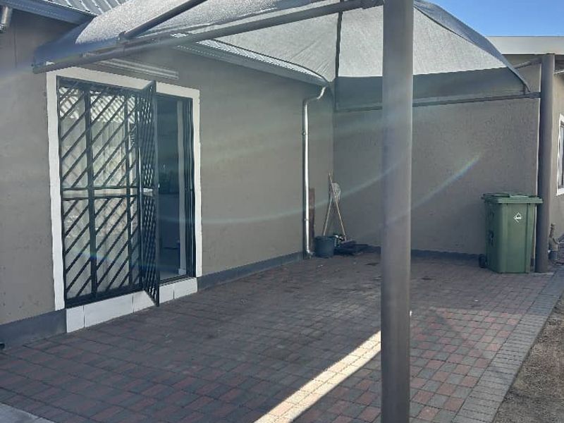 A paved outdoor patio area featuring a shade sail structure and a security gate entrance to the apartment.