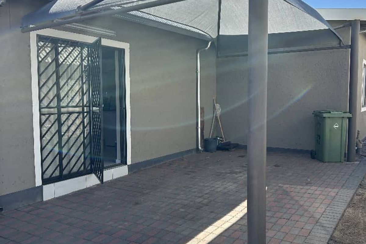 A paved outdoor patio area featuring a shade sail structure and a security gate entrance to the apartment.