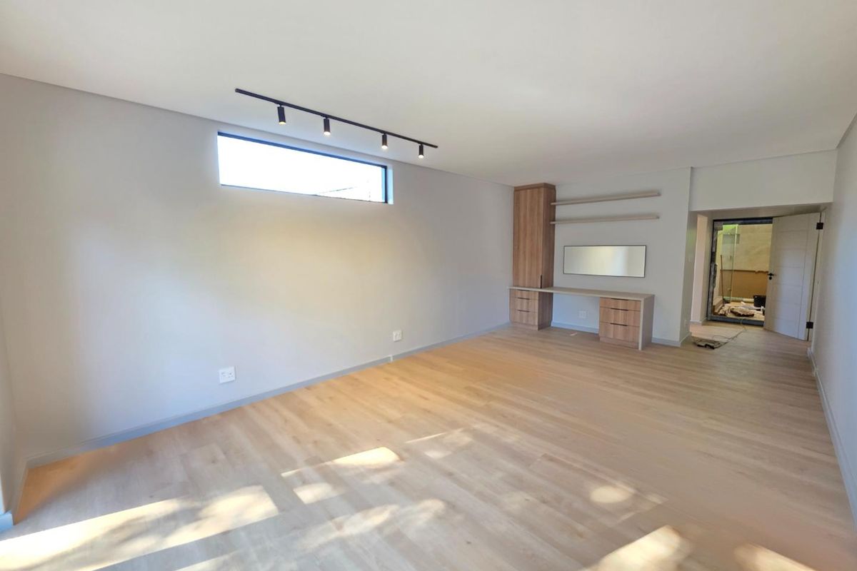 Spacious bedroom featuring light wood laminate flooring, modern track lighting, a built-in desk with cabinetry, and a sleek clerestory window.