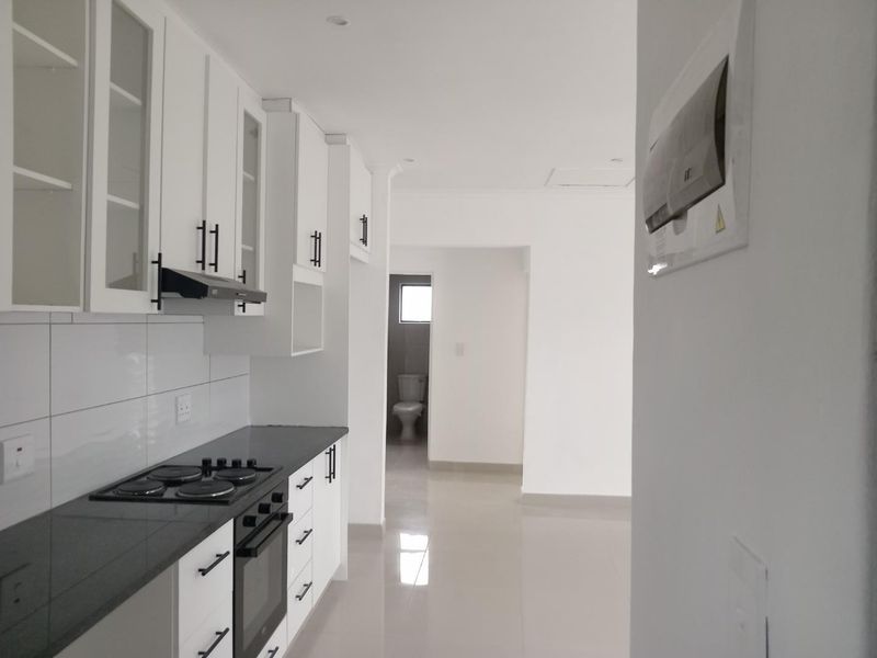 Modern kitchen featuring white cabinetry, dark stone countertops, built-in oven and hob, with a view through to an adjacent bathroom area.