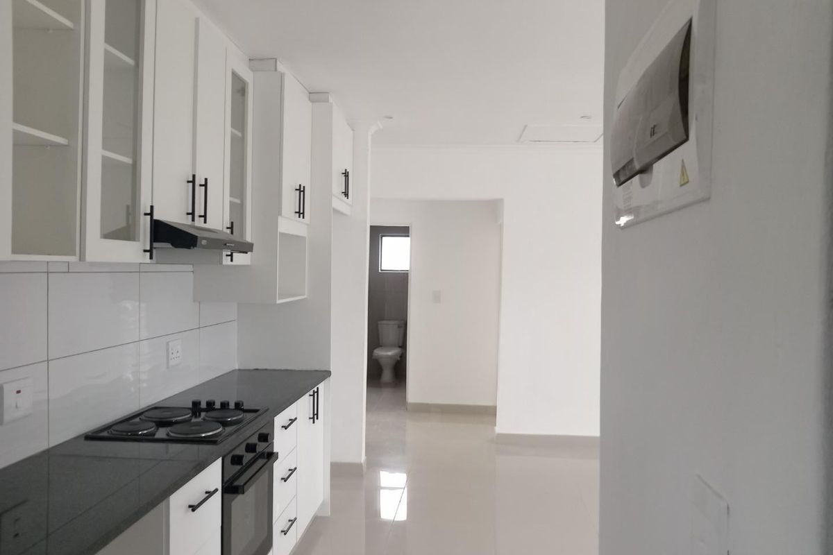 Modern kitchen featuring white cabinetry, dark stone countertops, built-in oven and hob, with a view through to an adjacent bathroom area.