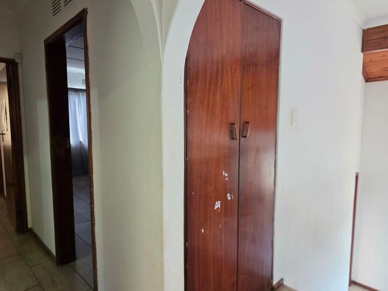 A hallway featuring tiled flooring, a built-in wooden cupboard, and a timber-paneled ceiling section, providing access to adjacent rooms.