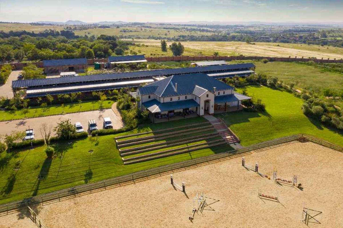 Aerial view of a large equestrian estate featuring a main residence, extensive stable blocks, and a professional sand riding arena.