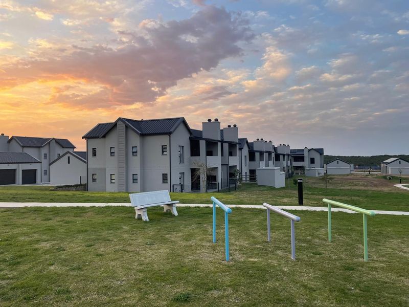 Exterior view of modern apartment complex buildings with metal roofing and plastered facades set against a sunset sky.