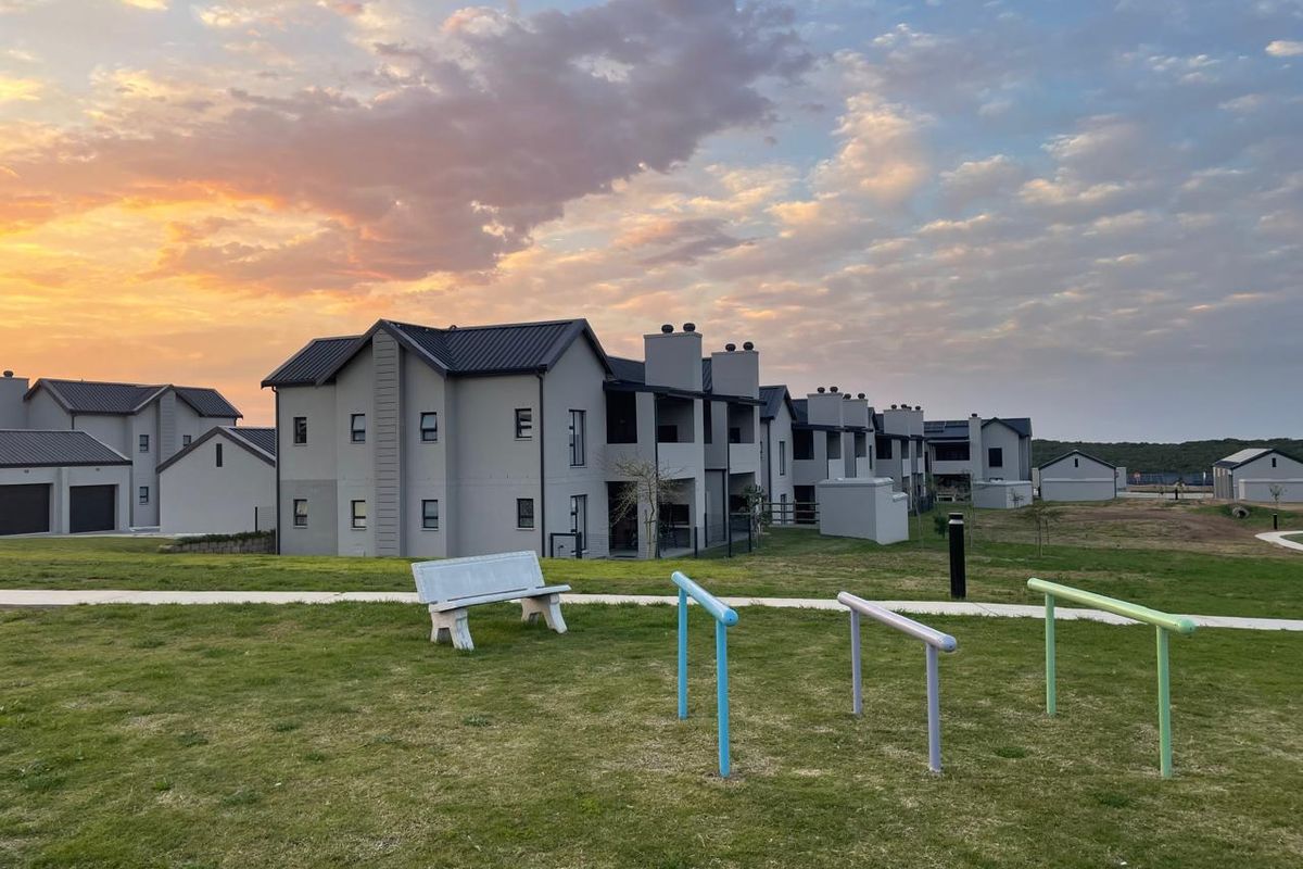 Exterior view of modern apartment complex buildings with metal roofing and plastered facades set against a sunset sky.