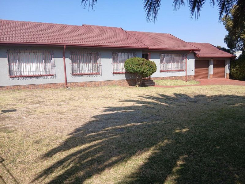 Front elevation of a single-story house featuring a tiled roof, brick plinth, security bars on windows, and a double garage with a paved driveway.