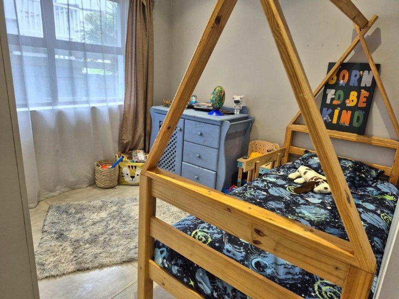 A functional bedroom featuring tiled flooring and a large window, providing natural light and a neutral base for personalization.