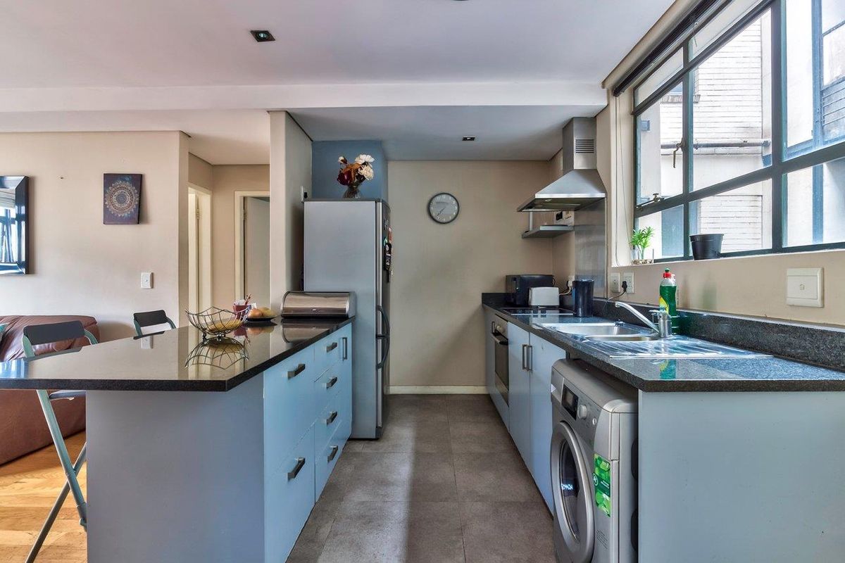 Modern kitchen featuring granite countertops, built-in oven, extractor fan, and integrated laundry space, offering a functional and well-lit cooking area.