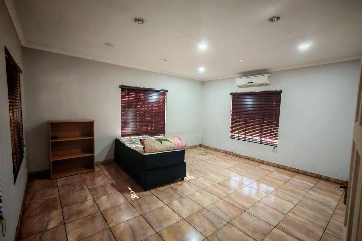 A spacious bedroom featuring tiled flooring, recessed ceiling lighting, and a wall-mounted air conditioning unit.