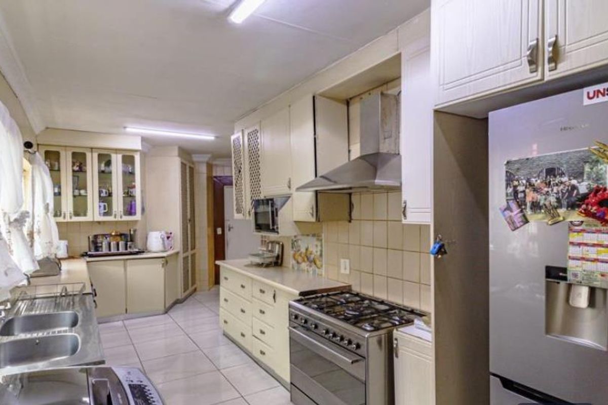 A functional kitchen featuring light-toned cabinetry, a stainless steel gas stove with extractor fan, double basin sink, and tiled flooring.