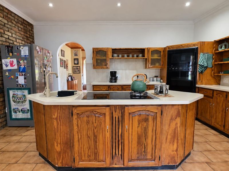 Spacious kitchen featuring a central island with built-in hob, wooden cabinetry, and a distinctive exposed brick feature wall.