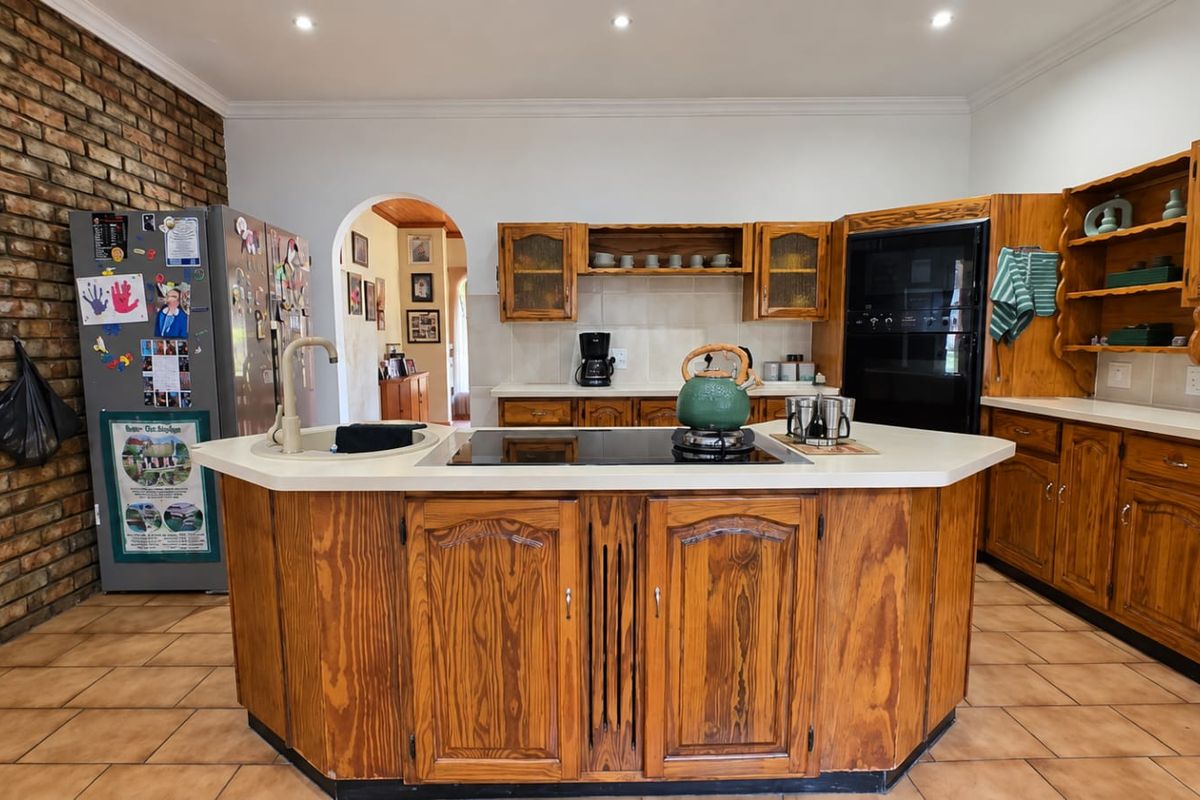 Spacious kitchen featuring a central island with built-in hob, wooden cabinetry, and a distinctive exposed brick feature wall.