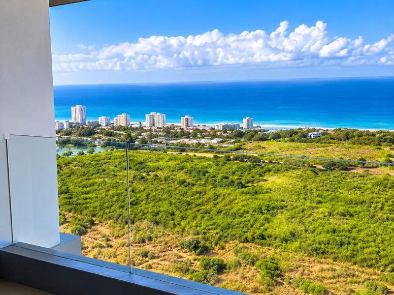 A modern covered balcony featuring a sleek glass balustrade and tiled flooring, offering expansive panoramic views of the coastline and surrounding landscape.