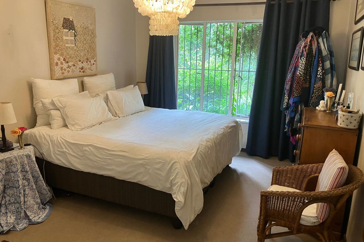 A comfortable bedroom featuring carpeted flooring, a large window with security bars, and a central light fixture.