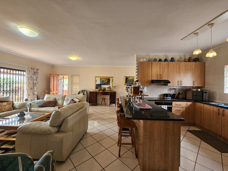 Spacious open-plan living area featuring a functional kitchen with wood cabinetry, granite countertops, and tiled flooring throughout, seamlessly connecting to the lounge space.