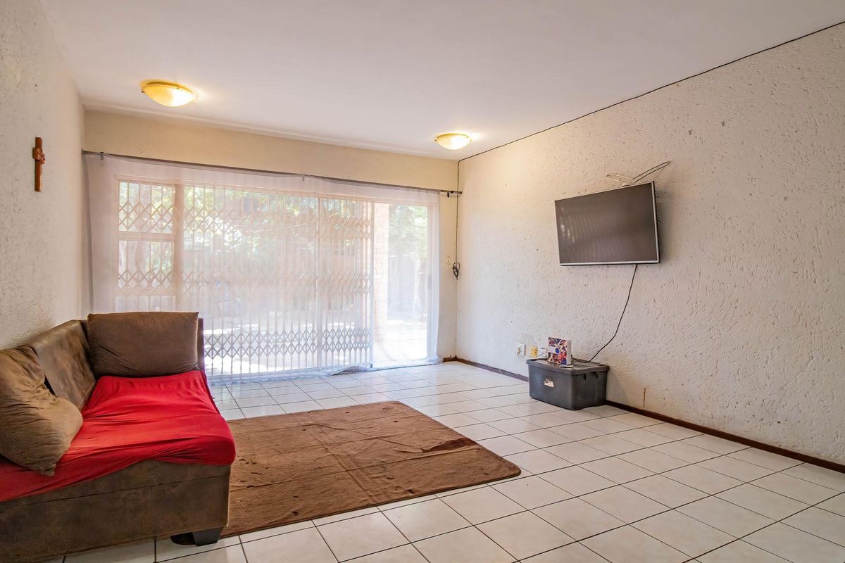 A living room featuring ceramic tile flooring and a sliding glass door with an integrated security gate, providing access to the exterior.