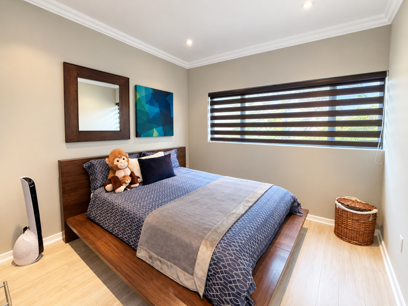 A well-maintained bedroom featuring light laminate flooring, crown molding, recessed lighting, and modern roller blinds for privacy.