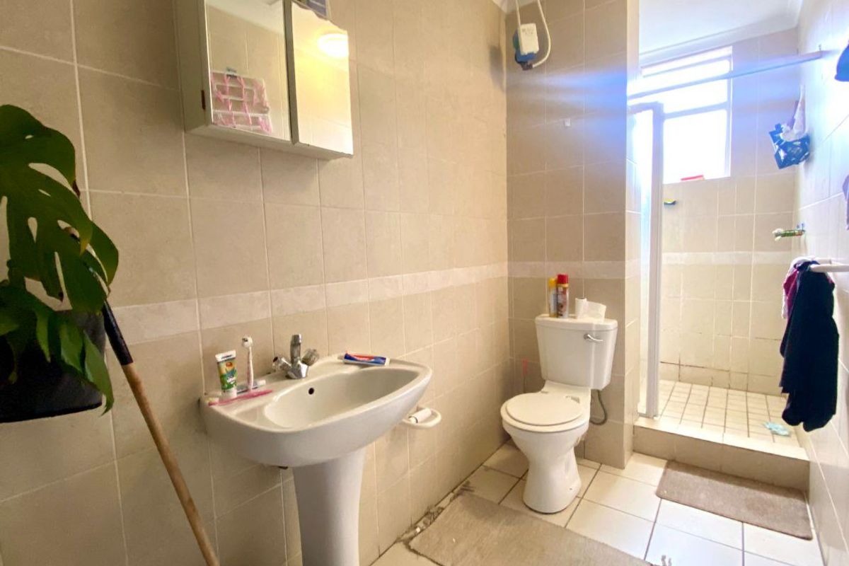 A functional bathroom featuring a pedestal washbasin, toilet, and a separate shower enclosure with neutral wall and floor tiling.