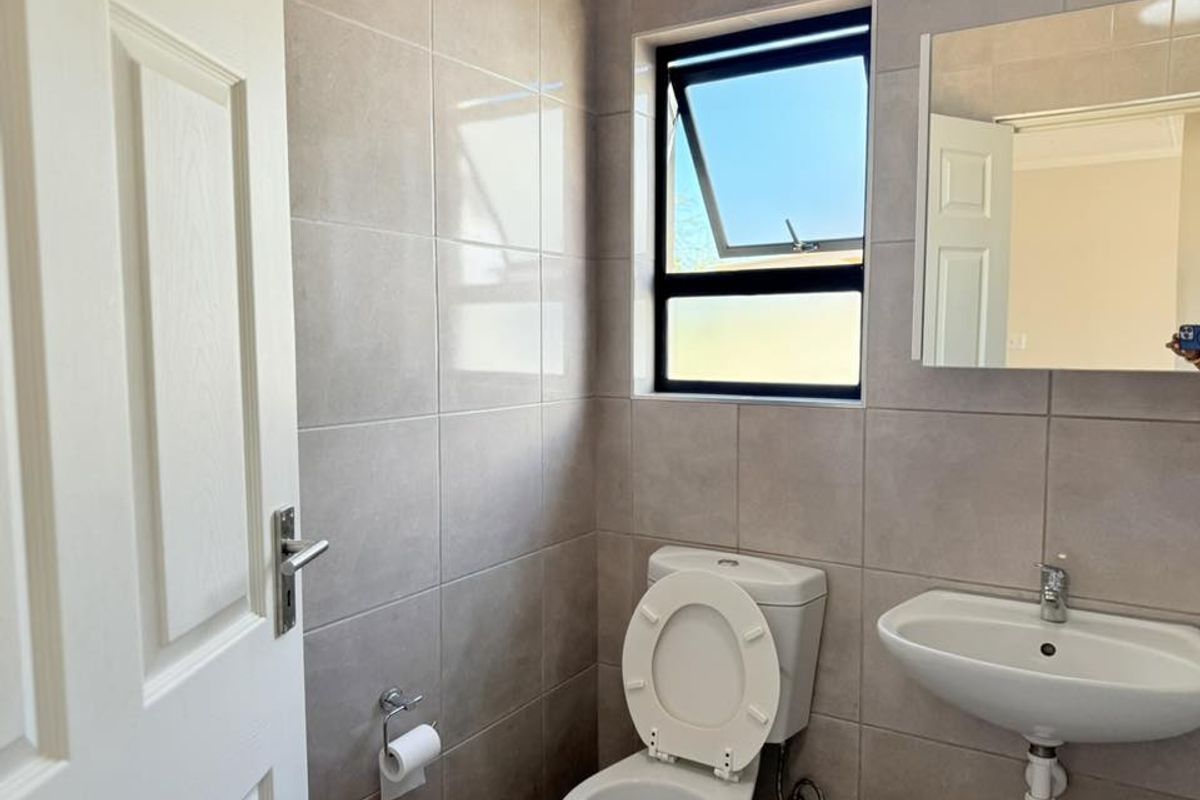 A clean, modern bathroom featuring neutral wall tiles, a wall-mounted mirror, a pedestal basin, and a standard toilet.