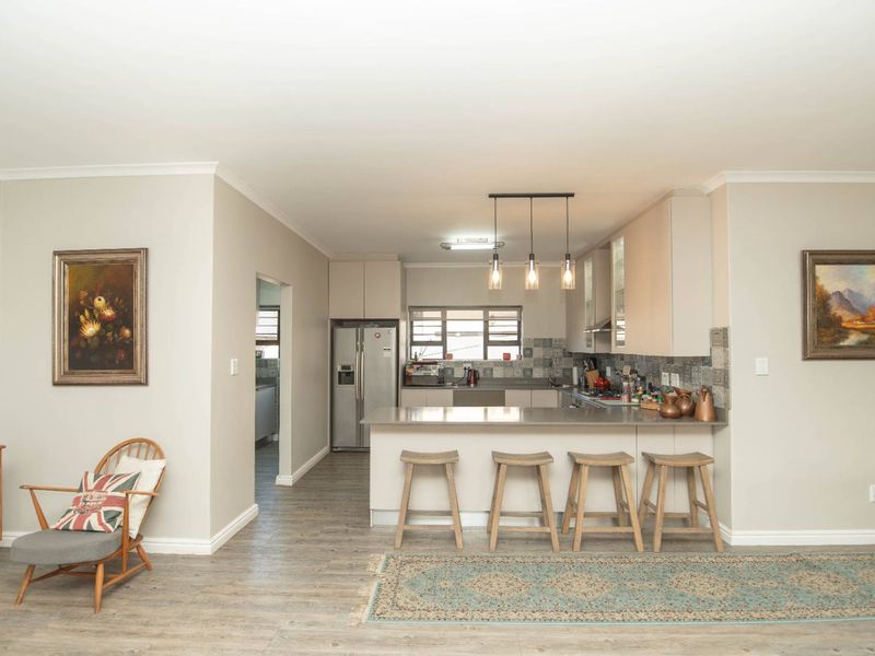 Modern open-plan kitchen featuring sleek cabinetry, stone countertops, a breakfast bar with pendant lighting, and durable laminate flooring.
