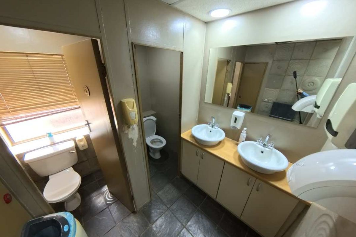 A functional office restroom featuring dual vanity basins, built-in cabinetry, and separate toilet cubicles with tiled flooring.