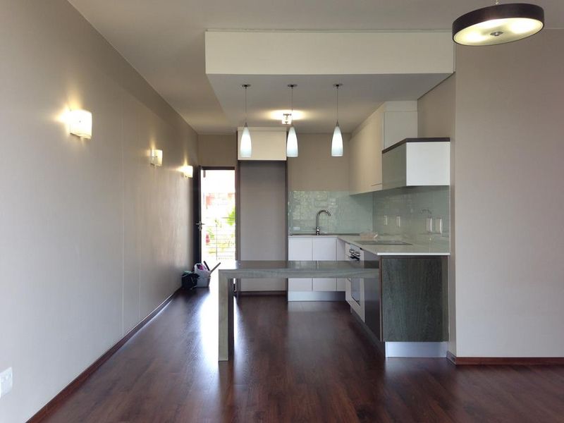 Modern open-plan kitchen and living area featuring sleek cabinetry, integrated appliances, pendant lighting, and dark laminate flooring leading to an outdoor balcony.