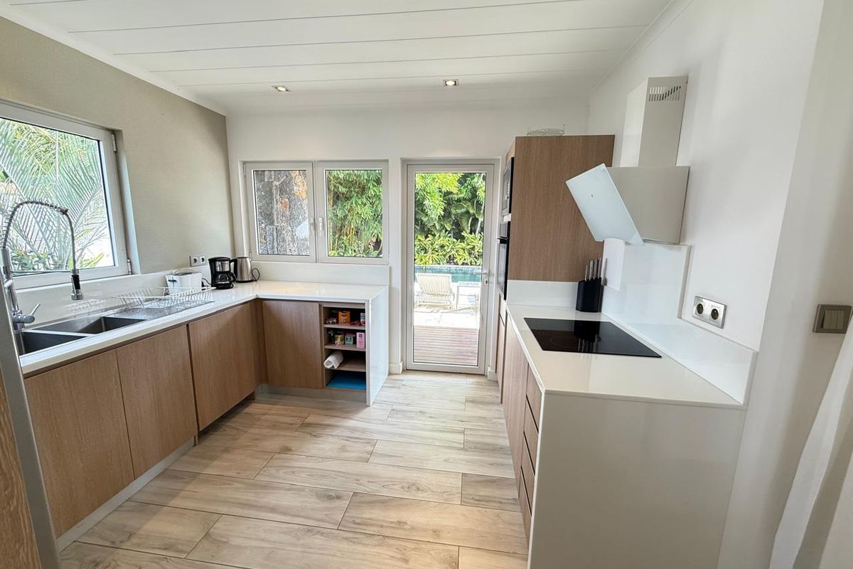 Modern kitchen featuring light wood cabinetry, white countertops, integrated induction hob, extractor fan, and direct access to the outdoor pool area.