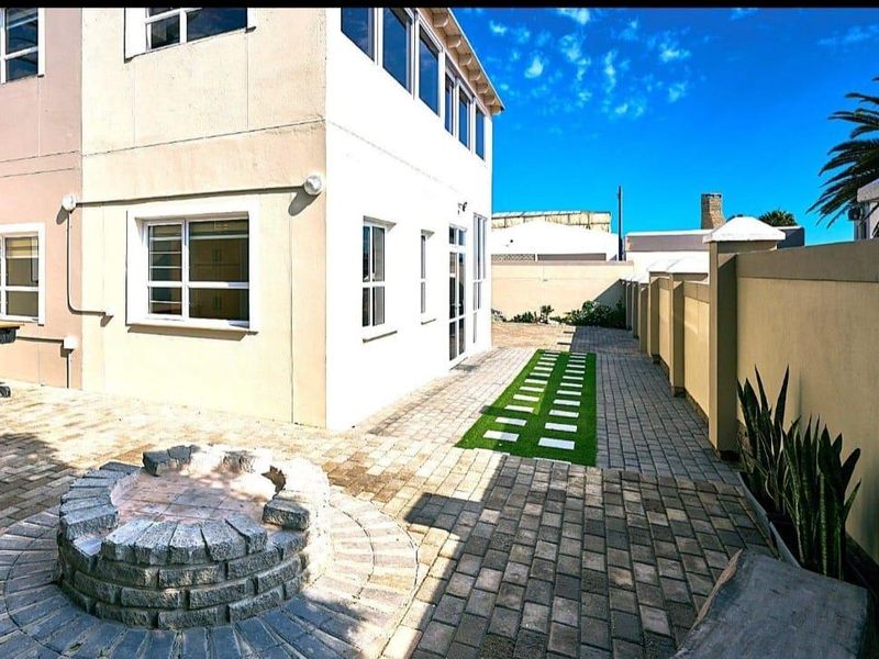 A well-maintained rear exterior area featuring a paved patio, a stone fire pit, and a boundary wall, providing a functional outdoor space.
